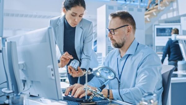 engineer holding electronic component and discussing alternatives with another engineer